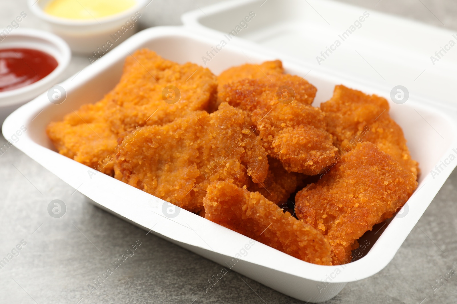 Photo of Delicious chicken nuggets in takeaway container on grey textured table, closeup