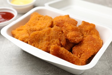 Photo of Delicious chicken nuggets in takeaway container on grey textured table, closeup