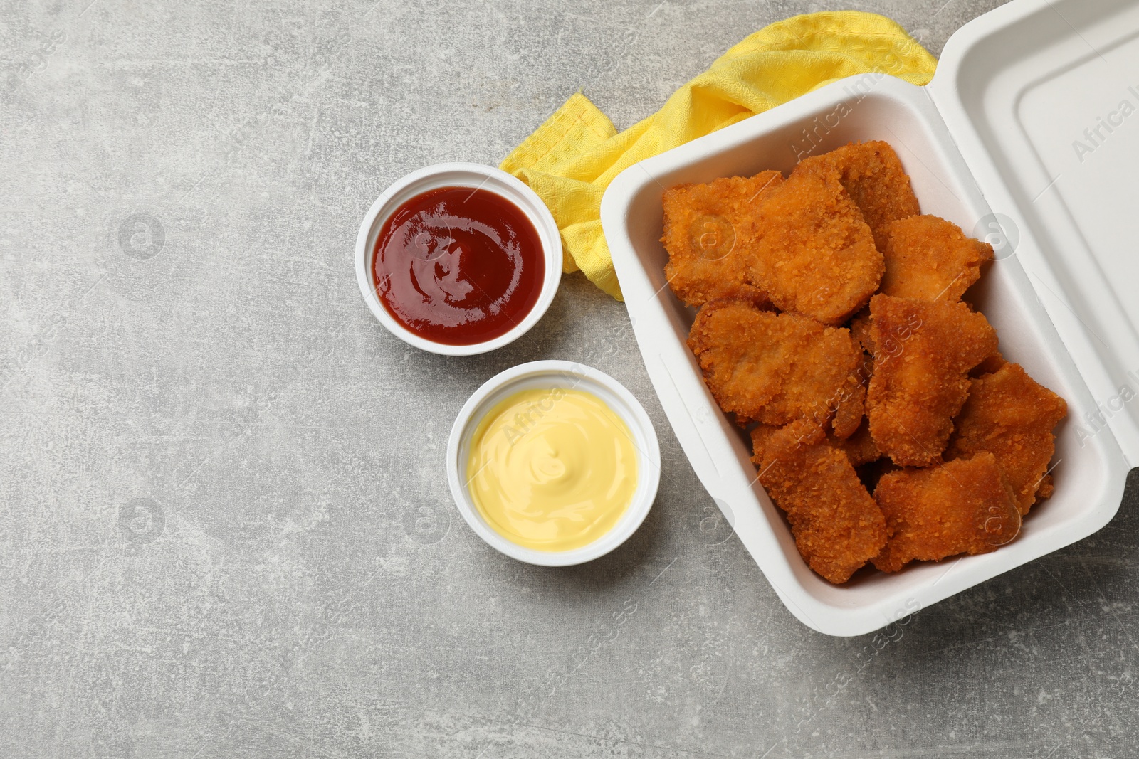 Photo of Delicious chicken nuggets in takeaway container with sauces on grey textured table, flat lay. Space for text