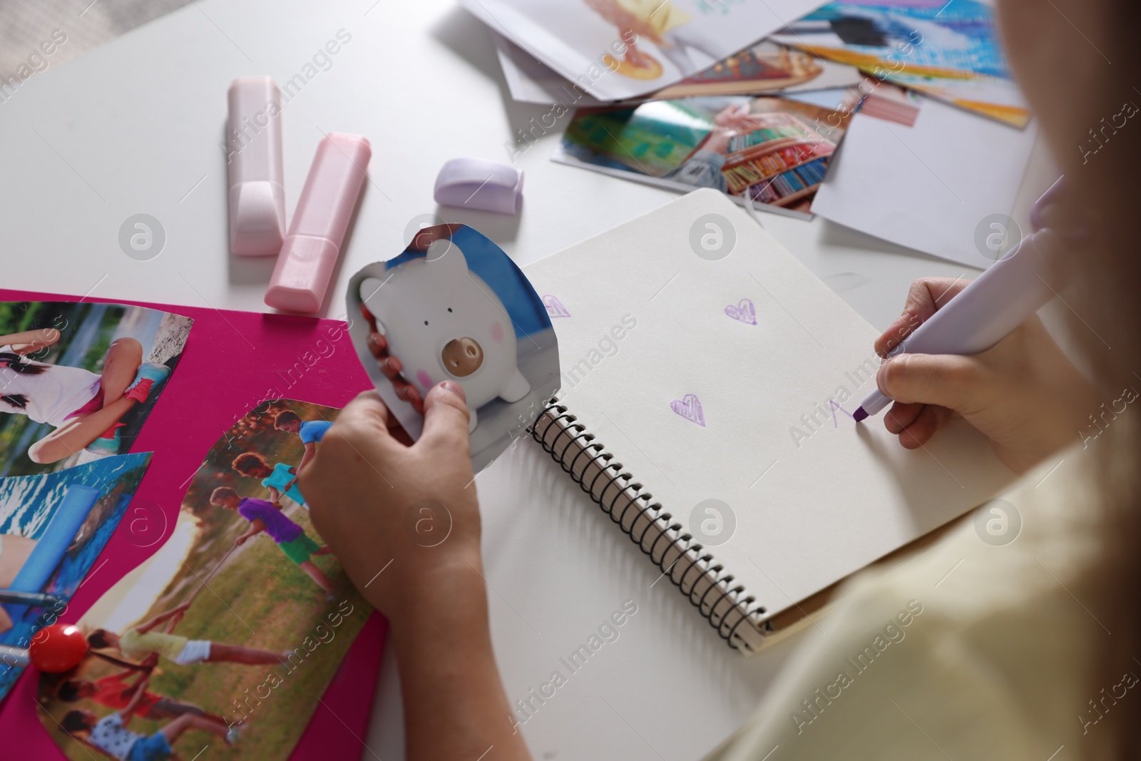 Photo of Creating vision board. Girl drawing violet hearts in notebook at light table, closeup