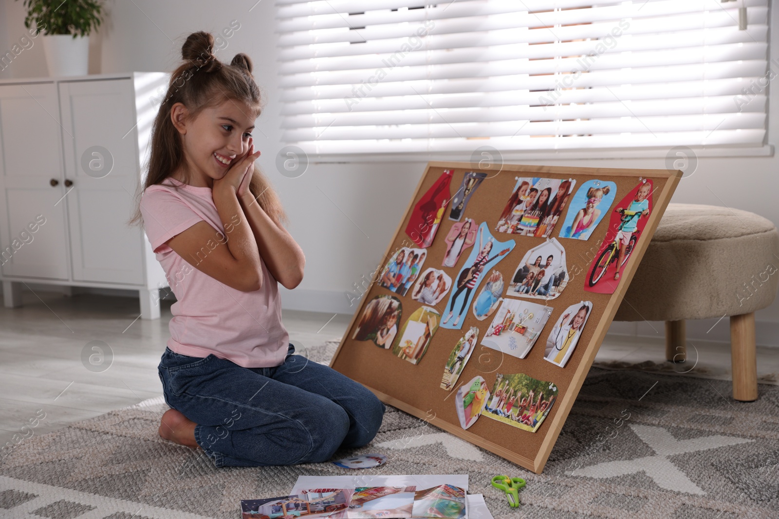 Photo of Happy girl looking at vision board with different pictures on floor indoors