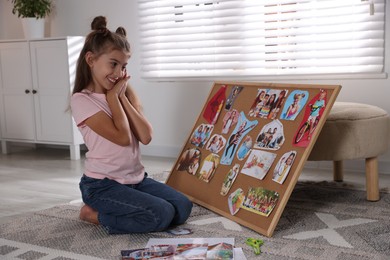 Photo of Happy girl looking at vision board with different pictures on floor indoors