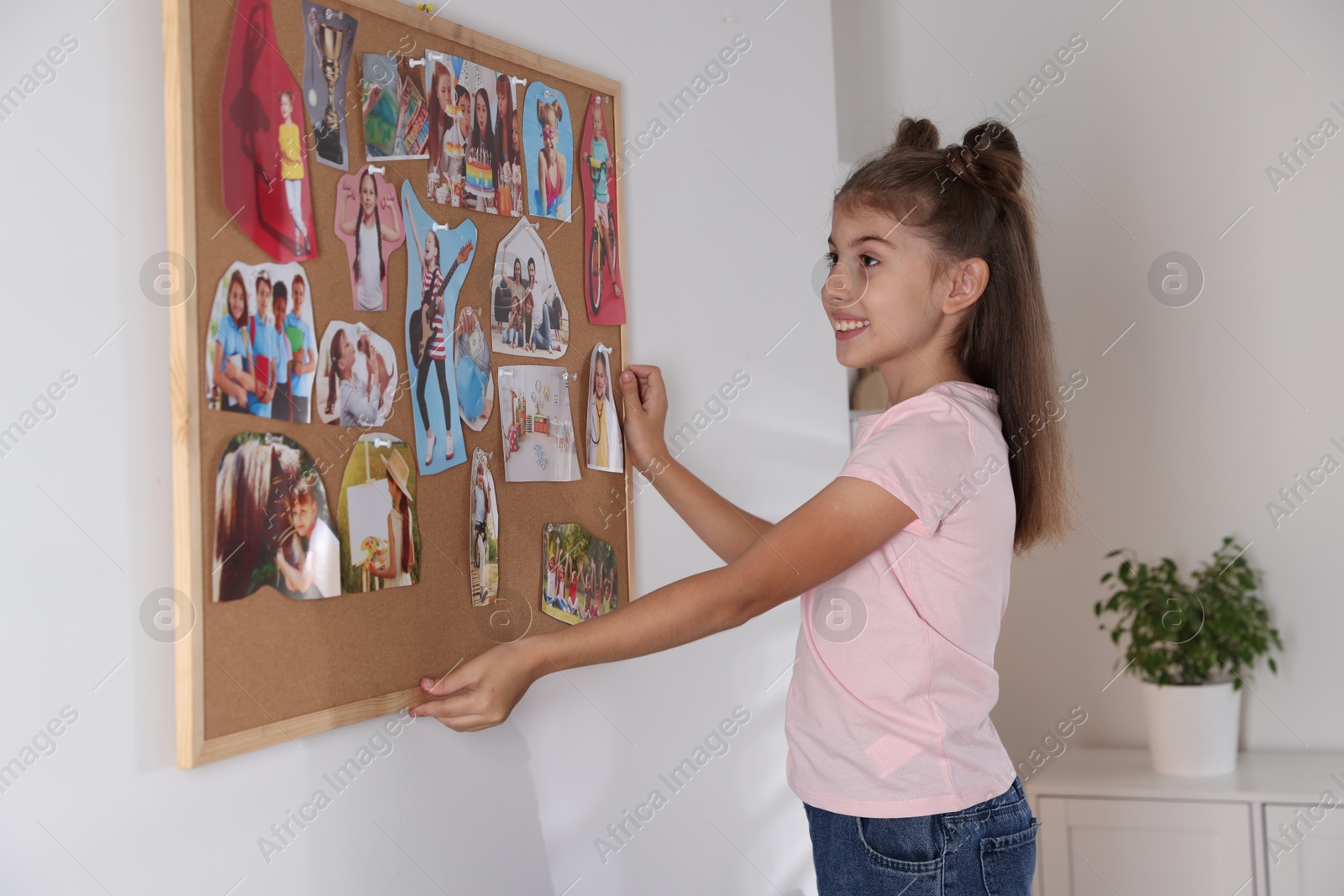 Photo of Girl hanging vision board with different pictures on wall indoors