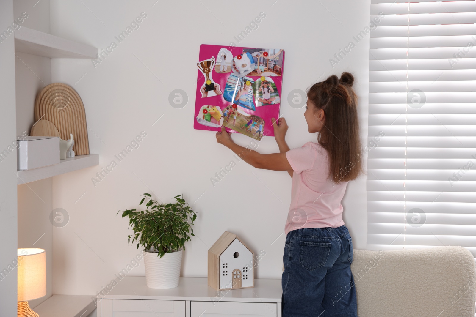 Photo of Girl hanging vision board with different pictures on wall indoors