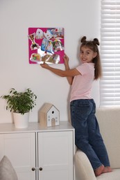 Girl hanging vision board with different pictures on wall indoors