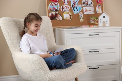 Creating vision board. Girl cutting out picture in armchair indoors