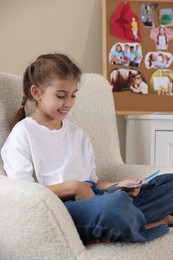 Creating vision board. Girl cutting out picture in armchair indoors