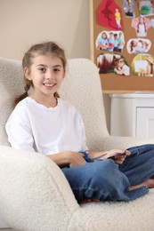 Creating vision board. Girl cutting out picture in armchair indoors