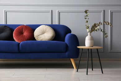 Image of Blue sofa with cushions and nesting table near grey wall in room