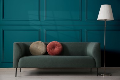 Image of Comfortable sofa with cushions and floor lamp near teal color wall in room