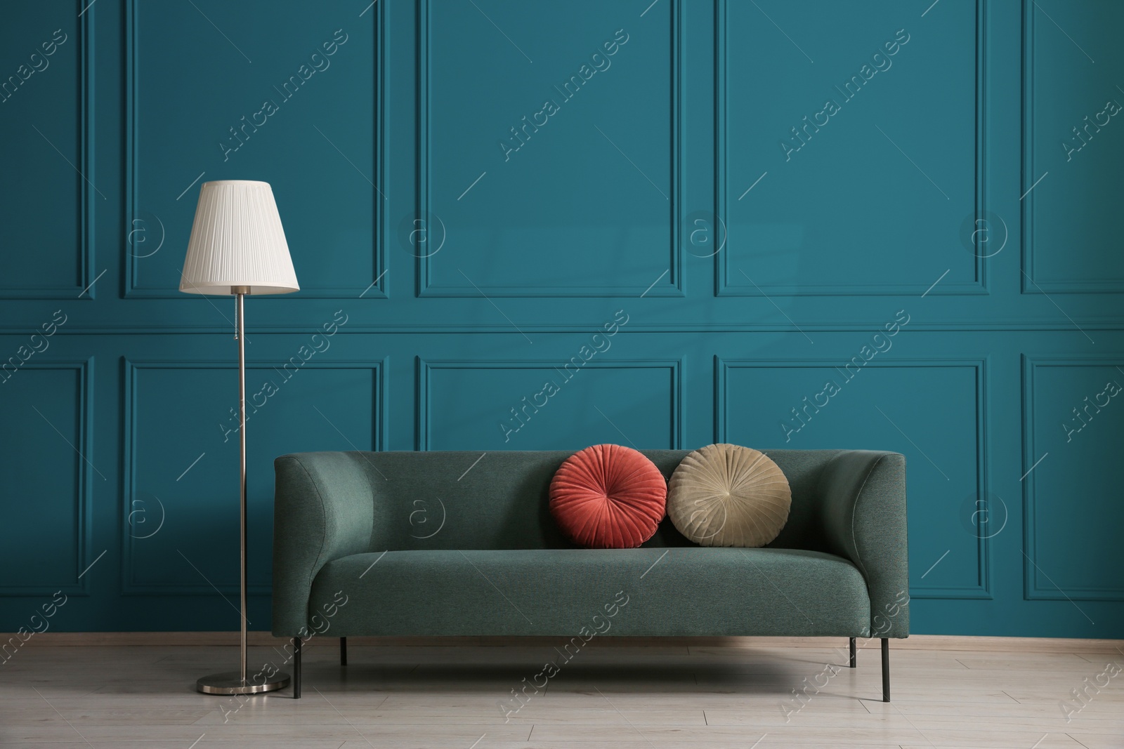 Image of Comfortable sofa with cushions and floor lamp near teal color wall in room