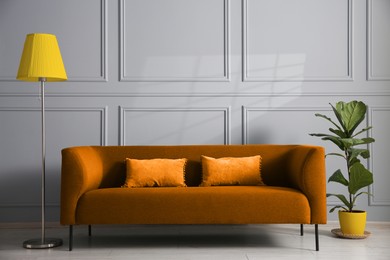 Image of Comfortable orange sofa, floor lamp and houseplant near light grey wall in room