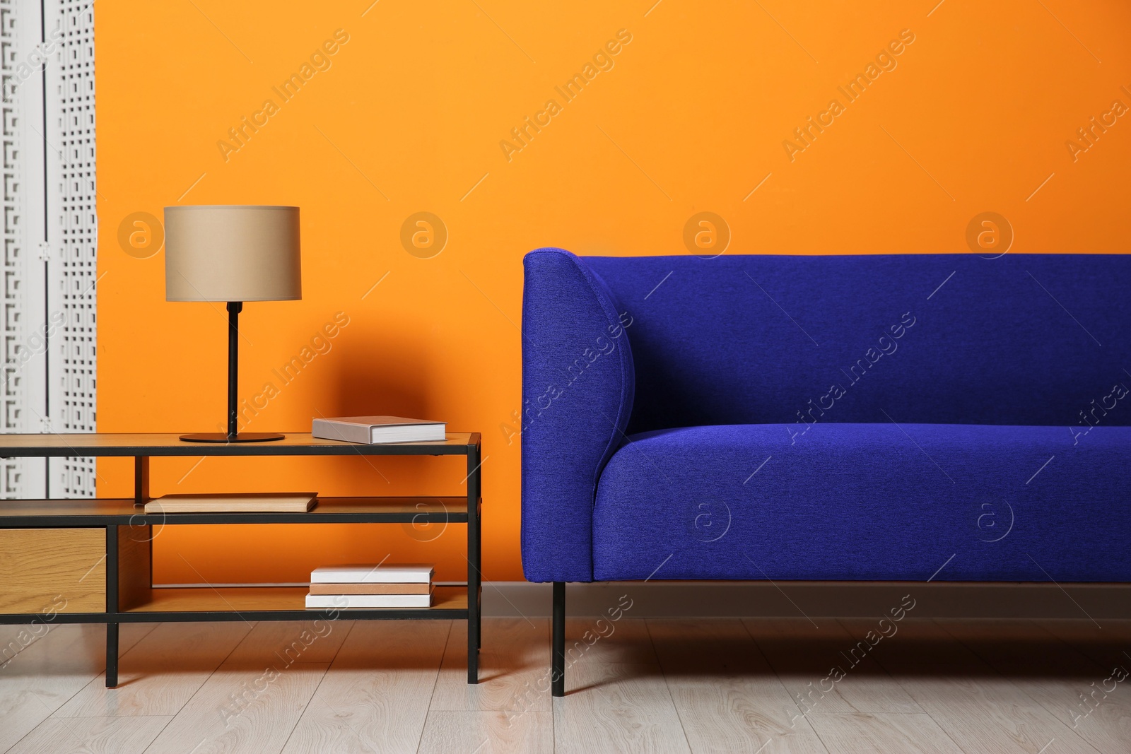 Image of Comfortable blue sofa and shelving unit near orange wall in room