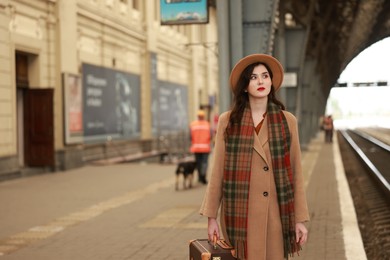 Photo of Beautiful woman with suitcase at railway station, space for text