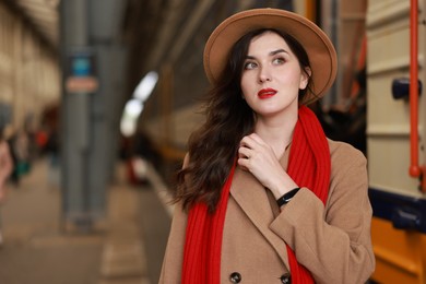 Photo of Woman with red scarf near train on platform of railway station, space for text