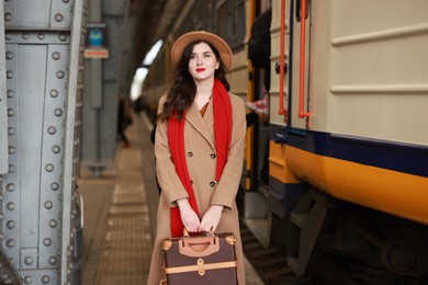 Woman with suitcase near train on platform of railway station