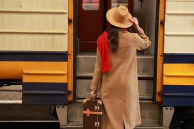 Photo of Woman with suitcase near train on platform of railway station, back view