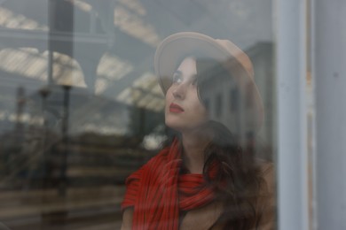 Photo of Woman with red scarf at railway station, view through glass window, space for text