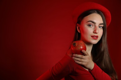 Woman with ripe pomegranate on red background, space for text