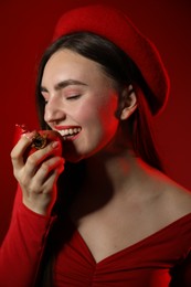 Woman eating ripe pomegranate on red background