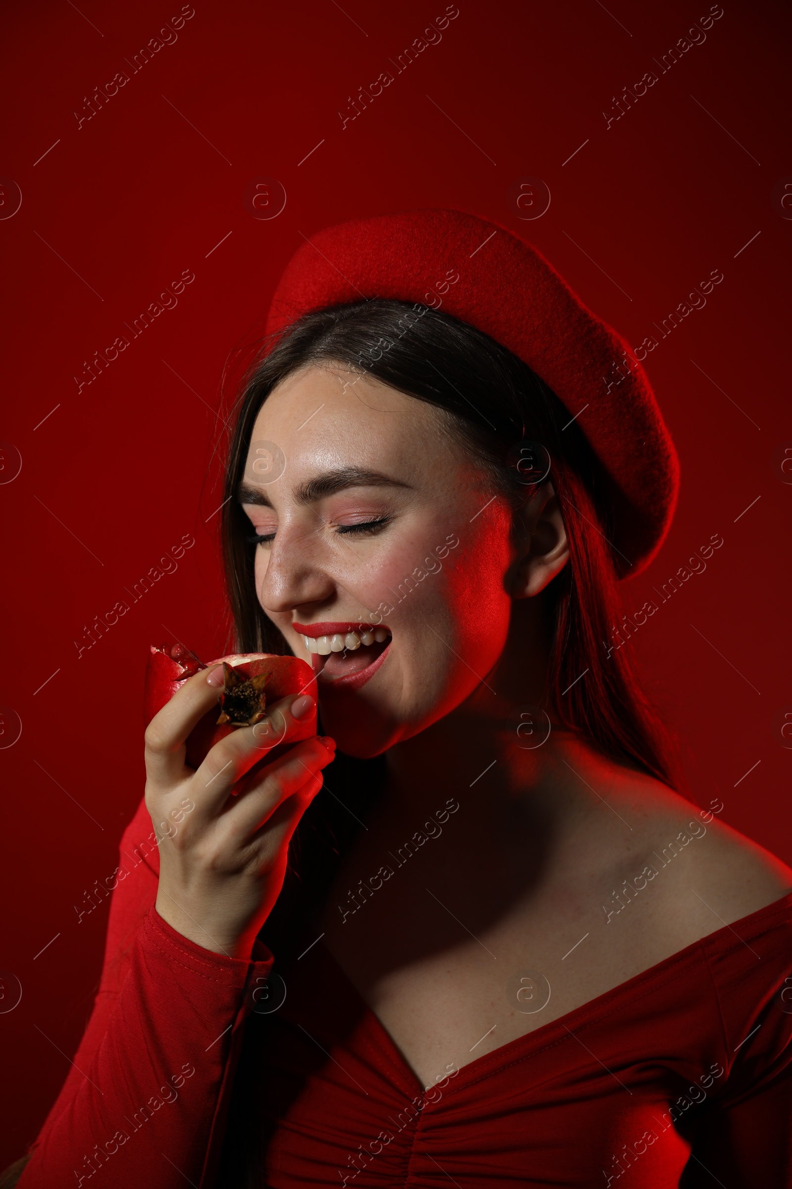 Photo of Woman eating ripe pomegranate on red background