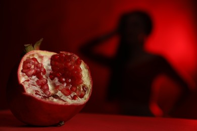 Photo of Woman posing against dark red background, focus on ripe pomegranate