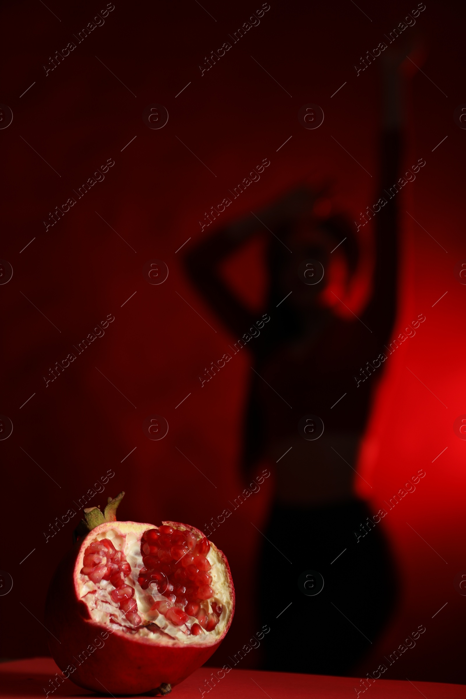 Photo of Woman posing against dark red background, focus on ripe pomegranate