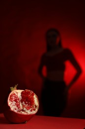 Photo of Woman posing against dark red background, focus on ripe pomegranate