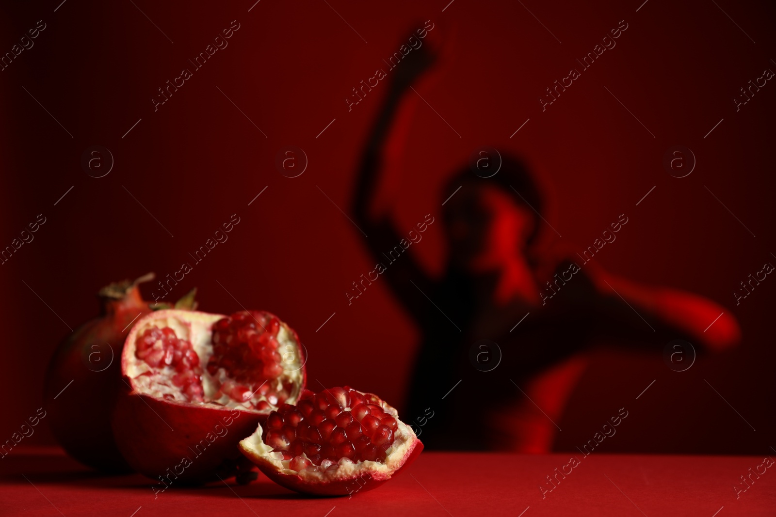 Photo of Woman posing against dark red background, focus on ripe pomegranate