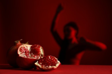 Woman posing against dark red background, focus on ripe pomegranate