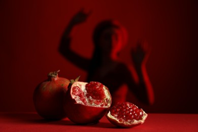 Woman posing against dark red background, focus on ripe pomegranate