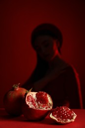 Woman posing against dark red background, focus on ripe pomegranate