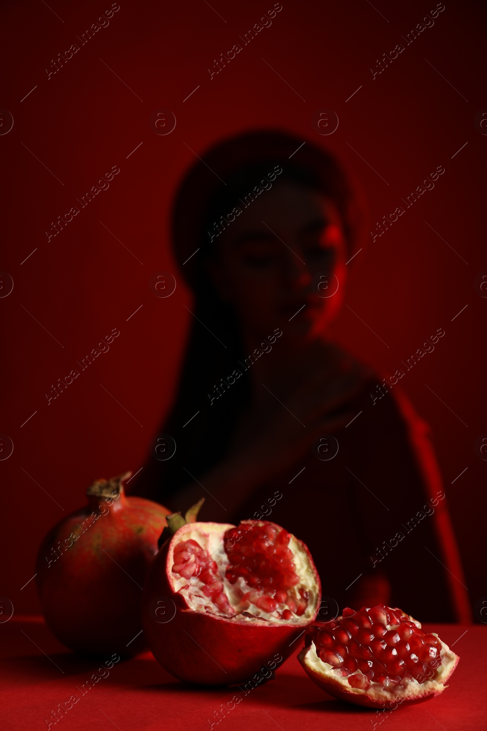 Photo of Woman posing against dark red background, focus on ripe pomegranate