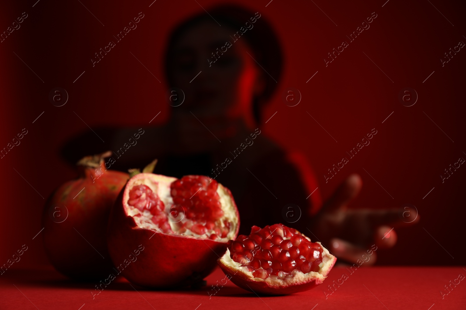 Photo of Woman posing against dark red background, focus on ripe pomegranate