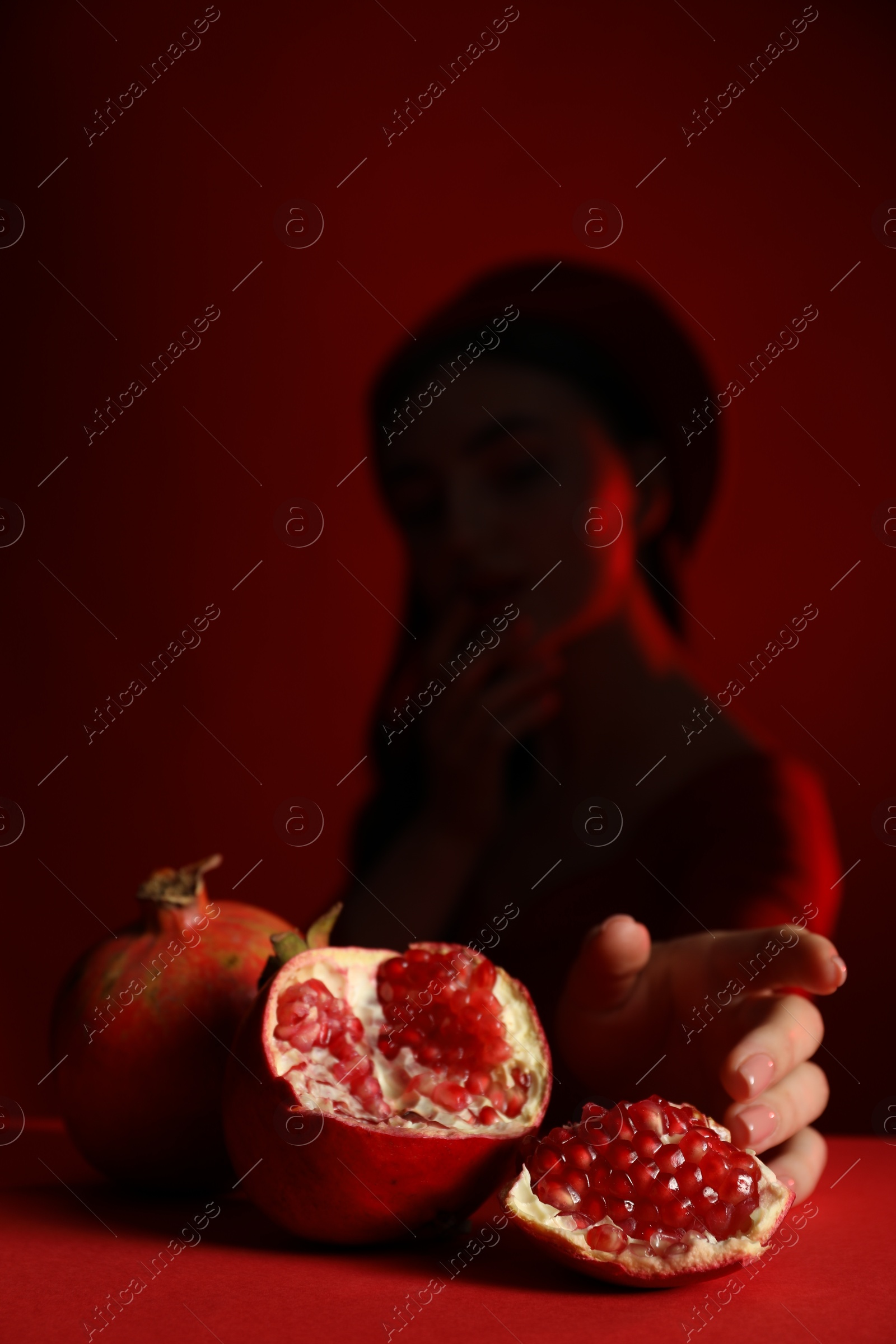 Photo of Woman posing against dark red background, focus on ripe pomegranate