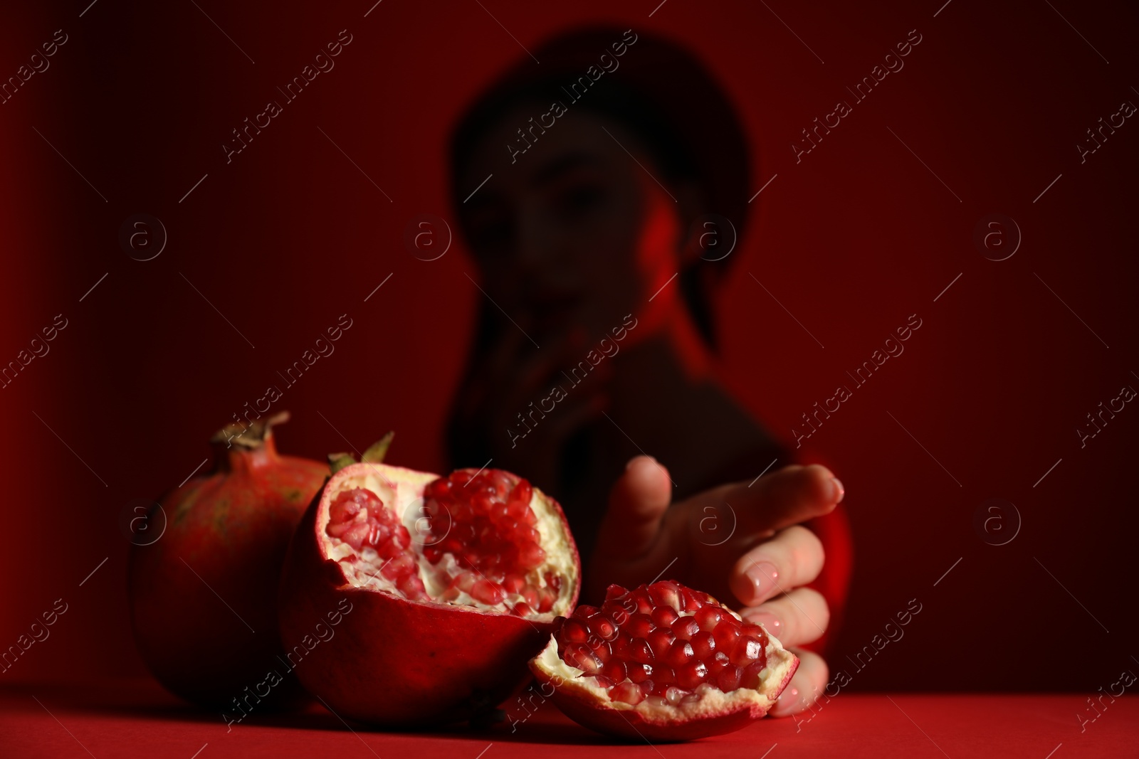 Photo of Woman posing against dark red background, focus on ripe pomegranate