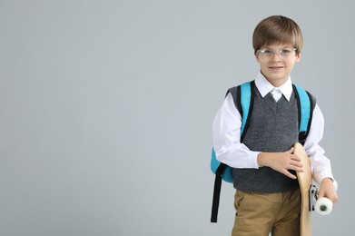 Little boy with skateboard on light grey background, space for text