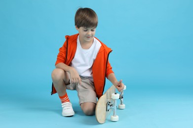 Little boy with skateboard on light blue background