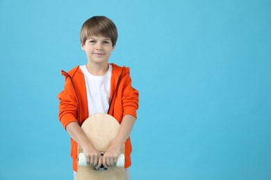 Little boy with skateboard on light blue background, space for text