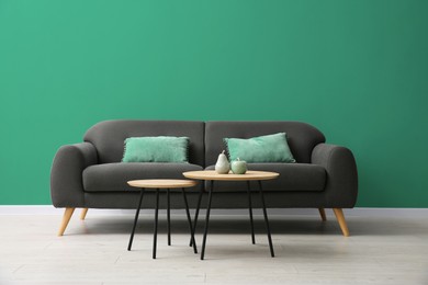 Image of Grey sofa and nesting tables near sea green color wall in room