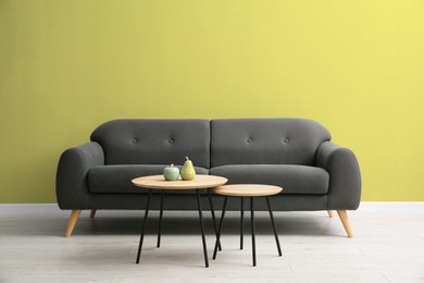 Image of Grey sofa and nesting tables near dusty yellow wall in room