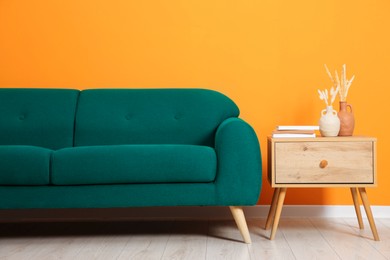 Image of Comfortable teal color sofa and side table near orange wall in room