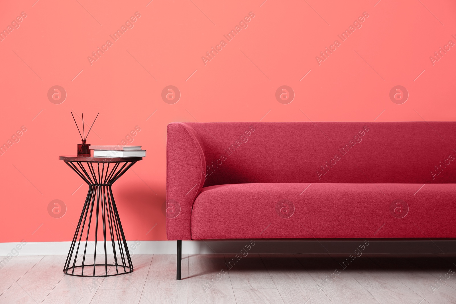 Image of Comfortable pink sofa and table near coral color wall in room