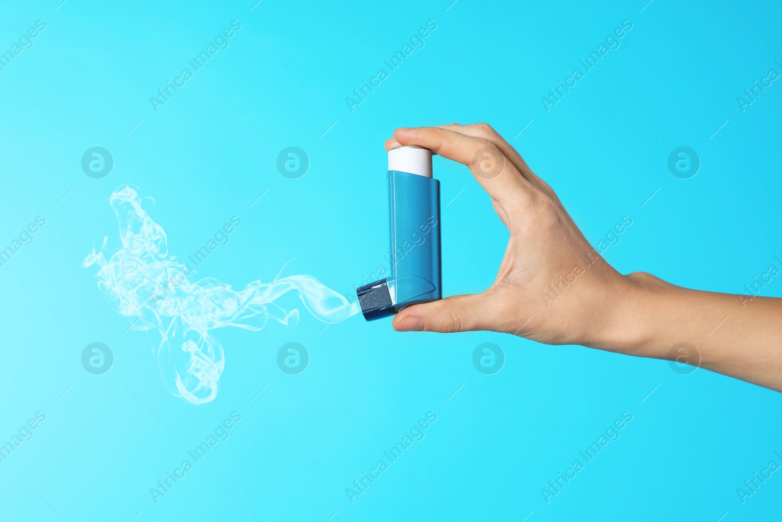 Image of Asthma treatment. Woman holding inhaler on light blue background, closeup. Aerosolized medication coming out of device