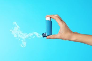 Image of Asthma treatment. Woman holding inhaler on light blue background, closeup. Aerosolized medication coming out of device