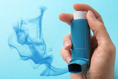 Asthma treatment. Woman holding inhaler on light blue background, closeup. Aerosolized medication coming out of device