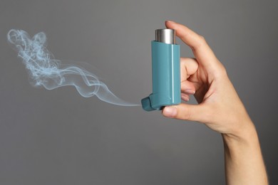 Asthma treatment. Woman holding inhaler on grey background, closeup. Aerosolized medication coming out of device