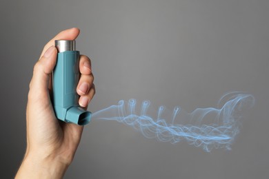 Image of Asthma treatment. Woman holding inhaler on grey background, closeup. Aerosolized medication coming out of device