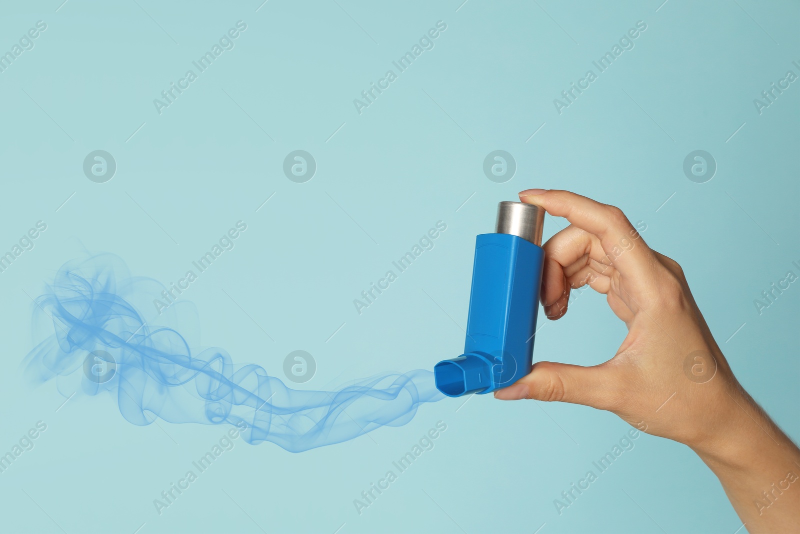 Image of Asthma treatment. Woman holding inhaler on light blue background, closeup. Aerosolized medication coming out of device