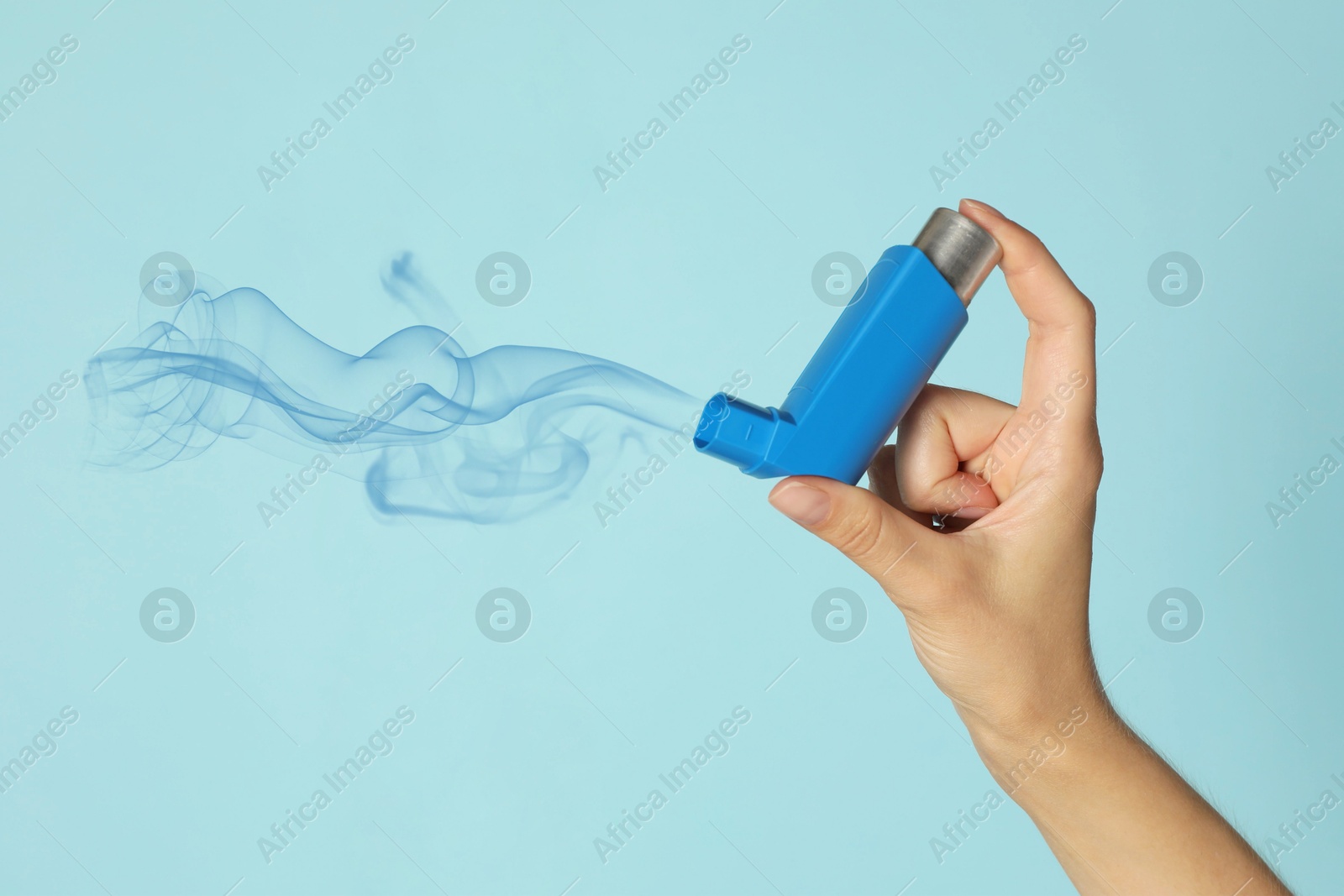 Image of Asthma treatment. Woman holding inhaler on light blue background, closeup. Aerosolized medication coming out of device